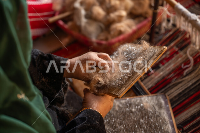 مهنه و حرفة يدوية تاريخيه, المحافظة على التراث السعودي، يوم بدينا 22 فبراير, ذكرى تأسيس الدولة السعودية الأولى 1727م, الاستعداد لنسج وغزل الخيوط, صورة مقربة لسيدة عربيه خليجية سعودية ترتدي العباءه السوداء تقوم بتمشيط الصوف