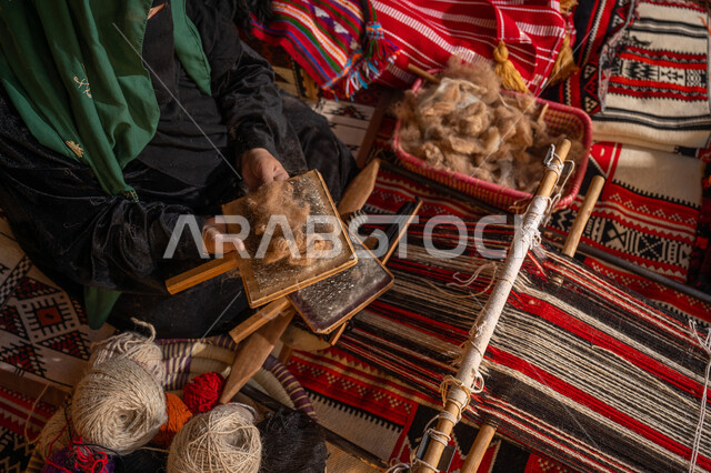 ذكرى تأسيس الدولة السعودية الأولى 1727م, الاستعداد لنسج وغزل الخيوط, حرفة و مهنة يدوية تاريخيه, المحافظة على التراث السعودي، يوم بدينا 22 فبراير, صورة من الاعلى لسيدة عربيه خليجية سعودية ترتدي العباءه السوداء و البرقع تقوم بتمشيط الصوف