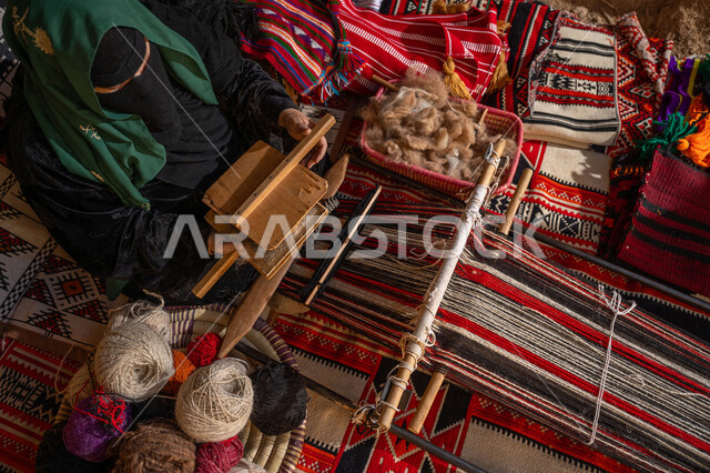 حرفة و مهنة يدوية تاريخيه, المحافظة على التراث السعودي، يوم بدينا 22 فبراير, ذكرى تأسيس الدولة السعودية الأولى 1727م, الاستعداد لنسج وغزل الخيوط, صورة من الاعلى لسيدة عربيه خليجية سعودية ترتدي العباءه السوداء و البرقع تقوم بتمشيط الصوف
