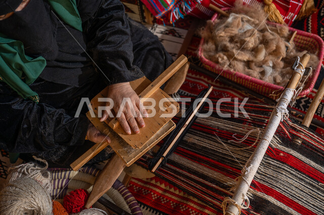 ذكرى تأسيس الدوله السعودية الأولى 1727م, الاستعداد لنسج وغزل الخيوط, حرفة و مهنة يدوية تاريخيه, المحافظة على التراث السعودي، يوم بدينا 22 فبراير, صورة من الاعلى لسيدة عربيه خليجية سعودية ترتدي العباءه السوداء و البرقع تقوم بتمشيط الصوف