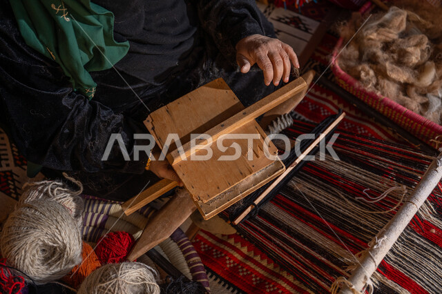 الاستعداد لنسج وغزل الخيوط, حرفة و مهنة يدوية تاريخيه, المحافظة على التراث السعودي، يوم بدينا 22 فبراير, ذكرى تأسيس الدولة السعودية الأولى 1727م, صورة مقربة من الاعلى لسيدة عربيه خليجية سعودية ترتدي العباءه السوداء تقوم بتمشيط الصوف