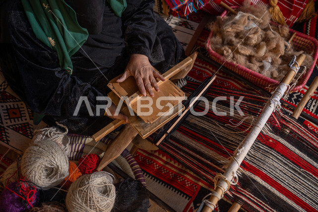 الاستعداد لنسج وغزل الخيوط, حرفة و مهنة يدوية تاريخيه, المحافظة على التراث السعودي، يوم بدينا 22 فبراير, ذكرى تأسيس الدولة السعودية الأولى 1727م, صورة مقربة من الاعلى لسيدة عربيه خليجية سعودية ترتدي العباءه السوداء تقوم بتمشيط الصوف
