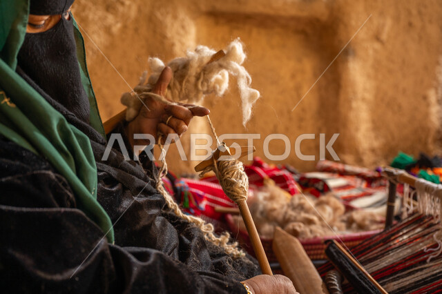 حرفة يدوية تاريخيه, المحافظة على التراث الشعبي السعودي, الشغف في ممارسة مهنة الغزل و النسج, يوم بدينا 22 فبراير, ذكرى تأسيس الدولة السعودية الأولى 1727م, صورة مقربة من الجانب لامرأة عربيه خليجية سعودية ترتدي البرقع و العباءه السوداء تقوم بلف خيوط الصوف