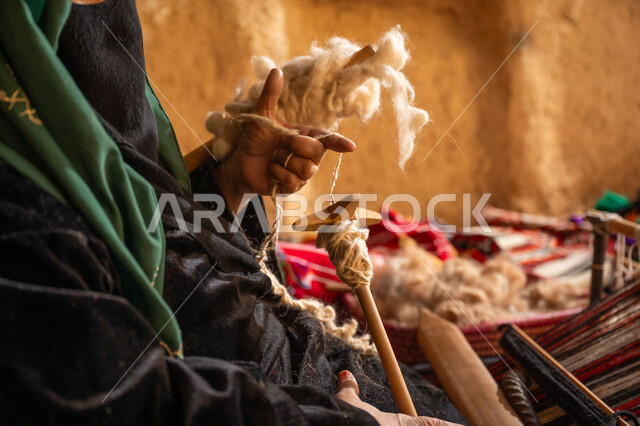 يوم بدينا 22 فبراير, ذكرى تأسيس الدولة السعودية الأولى 1727م, حرفة يدوية تاريخيه, المحافظة على التراث الشعبي السعودي, الشغف في ممارسة مهنة الغزل و النسج, صورة مقربة من الجانب لامرأة عربيه خليجية سعودية ترتدي البرقع و العباءه السوداء تقوم بلف خيوط الصوف