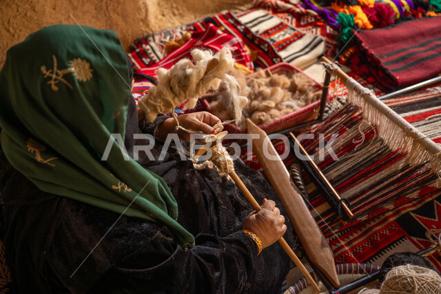 Passion for practicing the profession of spinning and weaving, the day we started February 22, the anniversary of the founding of the first Saudi state 1727 AD, a historical handicraft, preserving the Saudi folk heritage, a picture from above of a Saudi Gulf Arab woman wearing a black abaya twisting wool threads