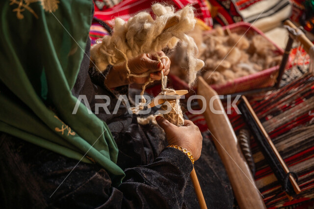 المحافظة على التراث الشعبي السعودي, يوم بدينا 22 فبراير, ذكرى تأسيس الدولة السعودية الأولى 1727م, حرفة يدوية تاريخيه, الشغف في ممارسة مهنة الغزل و النسج, صورة مقربة من الجانب لامرأة عربيه خليجية سعودية ترتدي البرقع و العباءه السوداء تقوم بلف خيوط الصوف