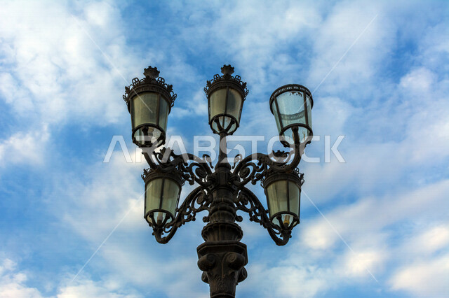 ضوء الشارع المعدني الأسود تحت السماء الزرقاء في المملكة العربية السعودية , منظر زاوية منخفضة للمصباح الكهربائي , عمود مصباح الشارع ، جمال السماء في المملكة العربية السعودية