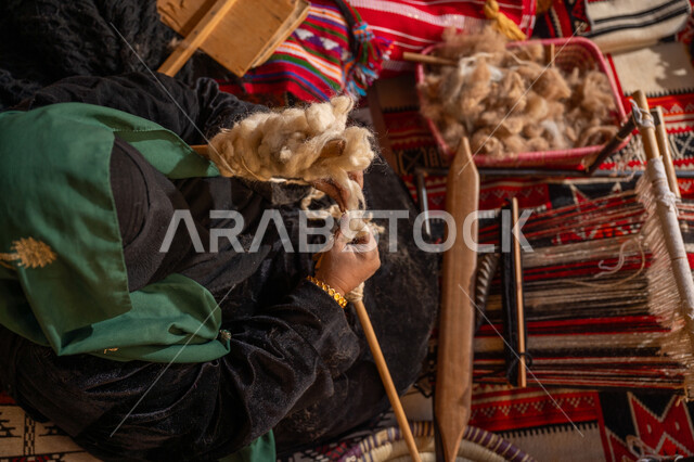 المحافظة على التراث الشعبي السعودي, يوم بدينا 22 فبراير, ذكرى تأسيس الدولة السعودية الأولى 1727م, الشغف في ممارسة مهنة الغزل و النسج, صورة من الاعلى لامرأة عربيه خليجية سعودية ترتدي البرقع و العباءه السوداء تقوم بلف خيوط الصوف, حرفة يدوية تاريخيه