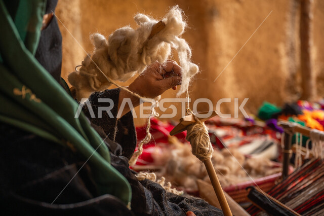 المحافظة على التراث الشعبي السعودي, يوم بدينا 22 فبراير, ذكرى تأسيس الدولة السعودية الأولى 1727م, حرفة يدوية تاريخيه, الشغف في ممارسة مهنة الغزل و النسج, صورة مقربة من الجانب لامرأة عربيه خليجية سعودية ترتدي البرقع و العباءه السوداء تقوم بلف خيوط الصوف