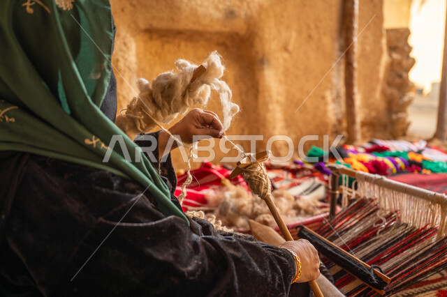 الشغف في ممارسة مهنة الغزل و النسج, المحافظة على التراث الشعبي السعودي, يوم بدينا 22 فبراير, ذكرى تأسيس الدولة السعودية الأولى 1727م, حرفة يدوية تاريخيه, صورة مقربة من الجانب لامرأة عربيه خليجية سعودية ترتدي البرقع و العباءه السوداء تقوم بلف خيوط الصوف