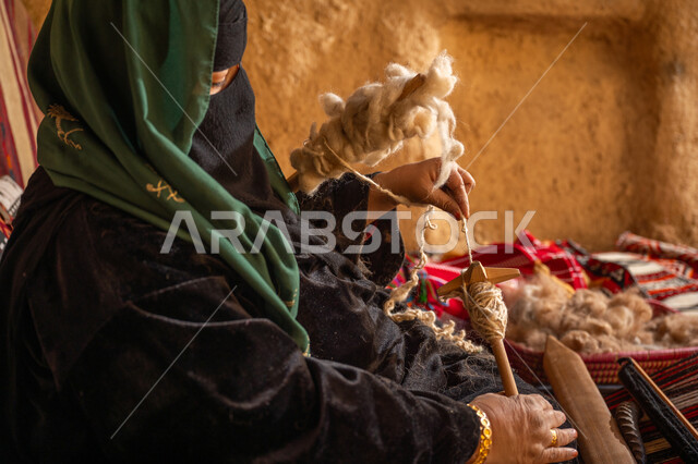 حرفة يدوية تاريخيه, الشغف في ممارسة مهنة الغزل و النسج, المحافظة على التراث الشعبي السعودي, يوم بدينا 22 فبراير, ذكرى تأسيس الدولة السعودية الأولى 1727م, صورة مقربة من الجانب لامرأة عربيه خليجية سعودية ترتدي البرقع و العباءه السوداء تقوم بلف خيوط الصوف