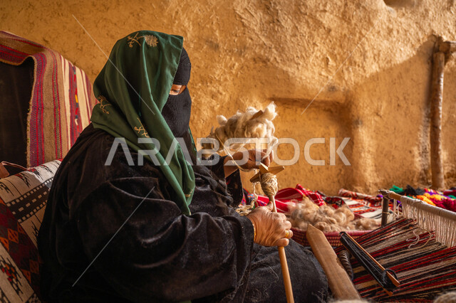 ذكرى تأسيس الدولة السعودية الأولى 1727م, حرفة يدوية تاريخيه, الشغف في ممارسة مهنة الغزل و النسج, المحافظة على التراث الشعبي السعودي, يوم بدينا 22 فبراير, صورة من الجانب لامرأة عربيه خليجية سعودية ترتدي البرقع و العباءه السوداء تقوم بلف خيوط الصوف