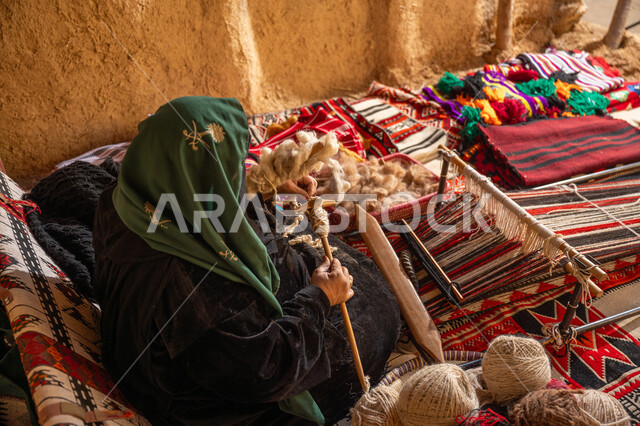 يوم بدينا 22 فبراير, المحافظة على التراث الشعبي السعودي, ذكرى تأسيس الدولة السعودية الأولى 1727م, حرفة يدوية تاريخيه, الشغف في ممارسة مهنة الغزل و النسج, صورة من الاعلى لامرأة عربيه خليجية سعودية ترتدي العباءه السوداء تقوم بلف خيوط الصوف