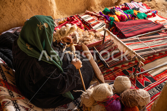المحافظة على التراث الشعبي السعودي, يوم بدينا 22 فبراير, ذكرى تأسيس الدولة السعودية الأولى 1727م, حرفة يدوية تاريخيه, الشغف في ممارسة مهنة الغزل و النسج, صورة من الاعلى لامرأة عربيه خليجية سعودية ترتدي العباءه السوداء تقوم بلف خيوط الصوف