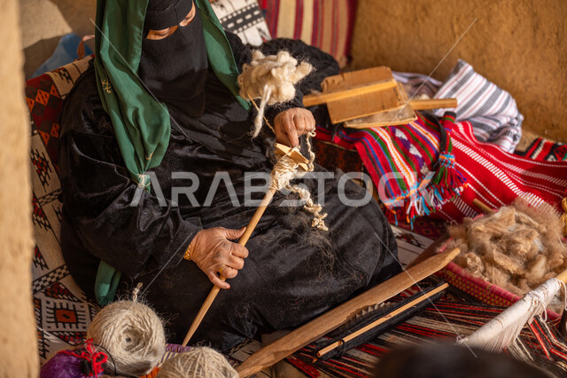 الشغف في ممارسة مهنة الغزل و النسج, يوم بدينا 22 فبراير, المحافظة على التراث الشعبي السعودي, ذكرى تأسيس الدولة السعودية الأولى 1727م, حرفة يدوية تاريخيه, امرأة عربيه خليجية سعودية ترتدي العباءه السوداء و البرقع تقوم بلف خيوط الصوف