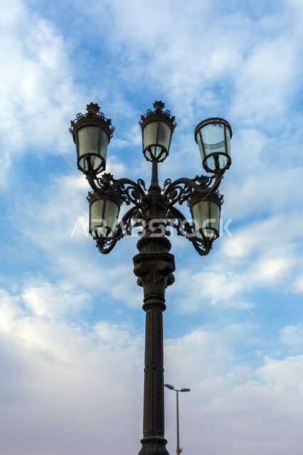 ضوء الشارع المعدني الأسود تحت السماء الزرقاء في المملكة العربية السعودية , منظر زاوية منخفضة للمصباح الكهربائي , عمود مصباح الشارع ، جمال السماء في المملكة العربية السعودية