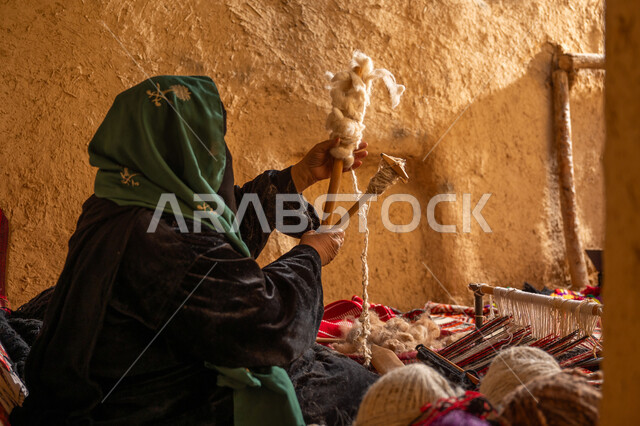 المحافظة على التراث الشعبي السعودي, يوم بدينا 22 فبراير, حرفة يدوية تاريخيه, الشغف في ممارسة مهنة الغزل و النسج, صورة من الجانب لامرأة عربيه خليجية سعودية ترتدي البرقع و العباءه السوداء تقوم بلف خيوط الصوف, ذكرى تأسيس الدولة السعودية الأولى 1727م