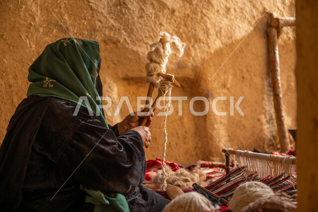 يوم بدينا 22 فبراير, حرفة يدوية تاريخيه, الشغف في ممارسة مهنة الغزل و النسج, المحافظة على التراث الشعبي السعودي, صورة من الجانب لامرأة عربيه خليجية سعودية ترتدي البرقع و العباءه السوداء تقوم بلف خيوط الصوف, ذكرى تأسيس الدولة السعودية الأولى 1727م