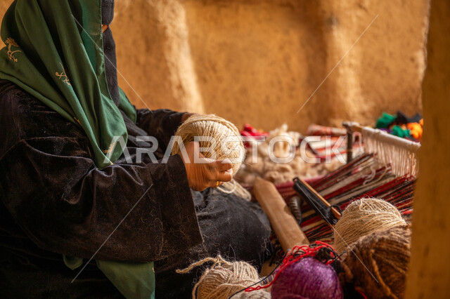 حرفة يدوية تاريخيه, يوم بدينا 22 فبراير، الشغف في ممارسة مهنة الغزل و النسج, المحافظة على التراث الشعبي السعودي, ذكرى تأسيس الدولة السعودية الأولى 1727م, صورة من الجانب لامرأة عربيه خليجية سعودية ترتدي البرقع و العباءه السوداء تقوم بلف خيوط الصوف