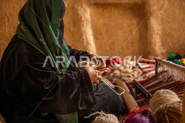 يوم بدينا 22 فبراير، الشغف في ممارسة مهنة الغزل و النسج, المحافظة على التراث الشعبي السعودي, حرفة يدوية تاريخيه, ذكرى تأسيس الدولة السعودية الأولى 1727م, صورة من الجانب لامرأة عربيه خليجية سعودية ترتدي البرقع و العباءه السوداء تقوم بلف خيوط الصوف