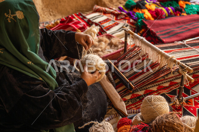 المحافظة على التراث الشعبي السعودي, حرفة يدوية تاريخيه, ذكرى تأسيس الدولة السعودية الأولى 1727م, الشغف في ممارسة مهنة الغزل و النسج, صورة من الاعلى لامرأة عربيه خليجية سعودية ترتدي البرقع و العباءه السوداء تقوم بلف خيوط الصوف, يوم بدينا 22 فبراير