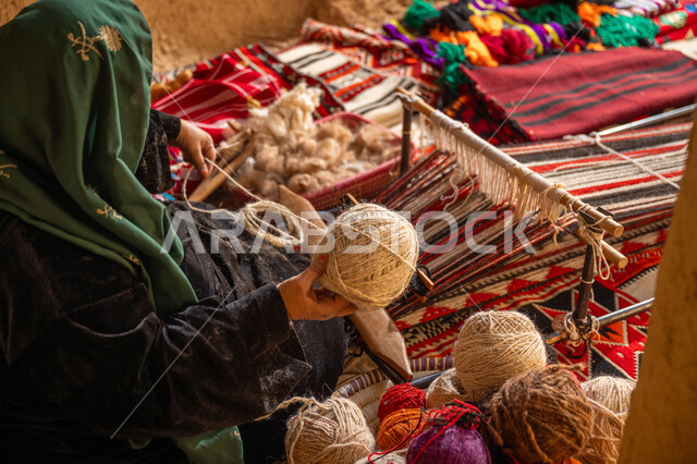 حرفة يدوية تاريخيه, ذكرى تأسيس الدولة السعودية الأولى 1727م, المحافظة على التراث الشعبي السعودي, الشغف في ممارسة مهنة الغزل و النسج, صورة من الاعلى لامرأة عربيه خليجية سعودية ترتدي البرقع و العباءه السوداء تقوم بلف خيوط الصوف, يوم بدينا 22 فبراير