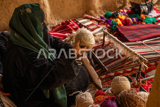 ذكرى تأسيس الدولة السعودية الأولى 1727م, المحافظة على التراث الشعبي السعودي, حرفة يدوية تاريخيه, الشغف في ممارسة مهنة الغزل و النسج, صورة من الجانب لامرأة عربيه خليجية سعودية ترتدي البرقع و العباءه السوداء تقوم بلف خيوط الصوف, يوم بدينا 22 فبراير