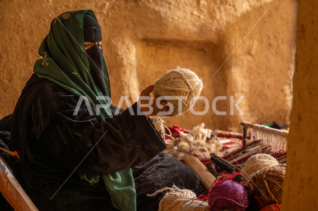 الشغف في ممارسة مهنة الغزل و النسج, المحافظة على التراث الشعبي السعودي, يوم بدينا 22 فبراير, ذكرى تأسيس الدولة السعودية الأولى 1727م, حرفة يدوية تاريخيه, صورة من الجانب لامرأة عربيه خليجية سعودية ترتدي البرقع و العباءه السوداء تقوم بلف خيوط الصوف