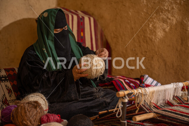 يوم بدينا 22 فبراير، الشغف في ممارسة مهنة الغزل و النسج, ذكرى تأسيس الدولة السعودية الأولى 1727م, المحافظة على التراث الشعبي السعودي, امرأة عربيه خليجية سعودية ترتدي البرقع و العباءه السوداء تقوم بلف خيوط الصوف, حرفة يدوية تاريخيه