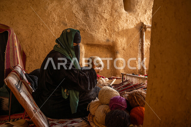 المحافظة على التراث الشعبي السعودي, يوم بدينا 22 فبراير, ذكرى تأسيس الدولة السعودية الأولى 1727م, حرفة يدوية تاريخيه, الشغف في ممارسة مهنة الغزل و النسج, صورة من الجانب لامرأة عربيه خليجية سعودية ترتدي البرقع و العباءه السوداء تقوم بلف خيوط الصوف