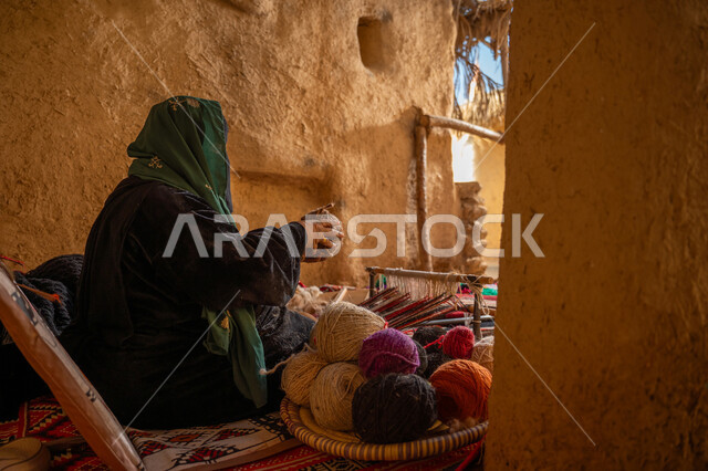 الشغف في ممارسة مهنة الغزل و النسج, المحافظة على التراث الشعبي السعودي, يوم بدينا 22 فبراير, ذكرى تأسيس الدولة السعودية الأولى 1727م, حرفة يدوية تاريخيه, صورة من الجانب لامرأة عربيه خليجية سعودية ترتدي البرقع و العباءه السوداء تقوم بلف خيوط الصوف