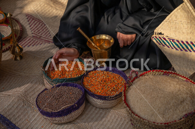 المحافظة على التراث السعودي، ذكرى تأسيس الدولة السعودية الأولى 1727م, عرض الحبوب والمنتج المحلي الوطني في سلل من الحصير اليدوي، صورة مقربة لبائعه عربيه خليجية سعودية ترتدي العباءه السوداء تقوم ببيع العدس و البقوليات على بساط شعبي، يوم بدينا 22 فبراير