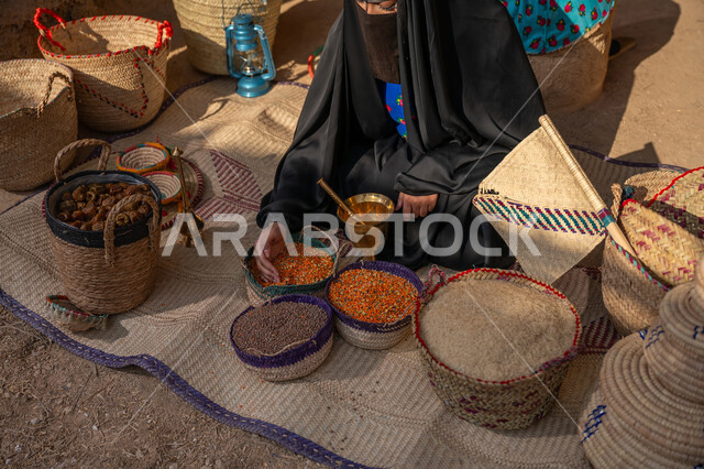 يوم بدينا 22 فبراير, ذكرى تأسيس الدولة السعودية الأولى 1727م, عرض الحبوب والمنتج المحلي الوطني في سلل من الحصير اليدوي، المحافظة على التراث السعودي ،صورة من الاعلى لبائعه عربيه خليجية سعودية ترتدي العباءه السوداء و البرقع تقوم ببيع العدس و البقوليات على بساط شعبي