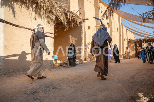 قماش ممتد بين البيوت لتوفير الظل، مجموعة من الأشخاص في سوق شعبي، يوم بدينا22 فبراير، ذكرى تأسيس الدولة السعودية الأولى1727 م، تجميع الحطب بموسم الشتاء, صورة مقربة من الخلف لرجل عربي خليجي سعودي يرتدي الثوب التقليدي والغترة يحمل أعواد الخشب في حي تاريخي