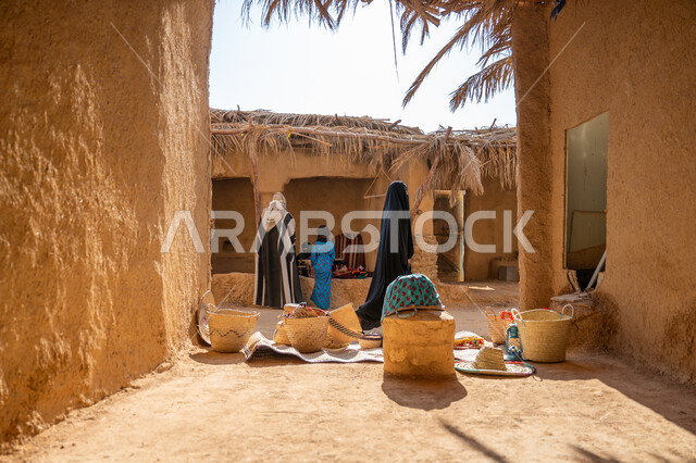 سوق شعبي تراثي، يوم بدينا 22 فبراير, ذكرى تأسيس الدولة السعودية الأولى 1727م، عرض منتج محلي وطني، قرية قديمة مبنية من الطوب، سلة من القش مصنوعة بشكل يدوي، صورة من الخلف لرجل عربي خليجي سعودي يرتدي الغترة والبشت يقف أمام منزل طيني قديم مغطى بسعائف الخوص الجاف