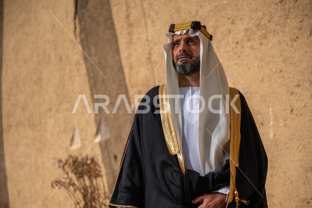 ذكرى تأسيس الدولة السعودية الأولى في 1727م، ارتداء الزي الشعبي في المناسبة الوطنية، الشموخ والاعتزاز والفخر، رجل عربي خليجي سعودي يرتدي الغترة والعقال الذهبي والبشت يقف أمام جدار طيني قديم, يوم بدينا 22 فبراير، إظهار حب الوطن والانتماء إليه