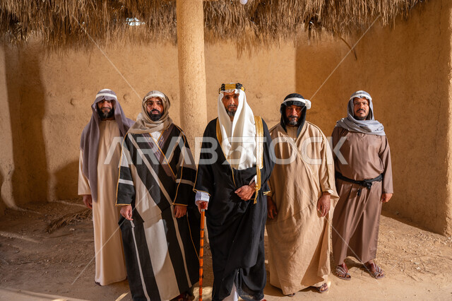 ذكرى تأسيس الدولة السعودية الأولى 1727م، يوم بدينا 22 فبراير, إيماءات الفخر بإنجازات المملكة، إظهار الولاء والحب للوطن, مجموعة رجال عرب خليجين سعوديين يرتدون الزي الشعبي التقليدي في المناسبة الوطنية يقفون في بيت من الطين قديم ينظرون إلى الكاميرا بتعابير الشموخ