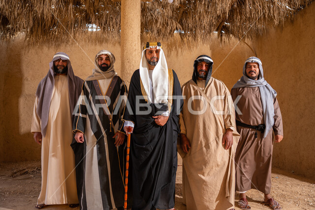 ذكرى تأسيس الدولة السعودية الأولى 1727م، إظهار الولاء والحب للوطن, مجموعة رجال عرب خليجين سعوديين يرتدون الزي الشعبي التقليدي في المناسبة الوطنية يقفون في بيت من الطين ينظرون إلى الكاميرا بتعابير الشموخ، إيماءات الثقة والفخر بإنجازات المملكة، يوم بدينا 22 فبراير