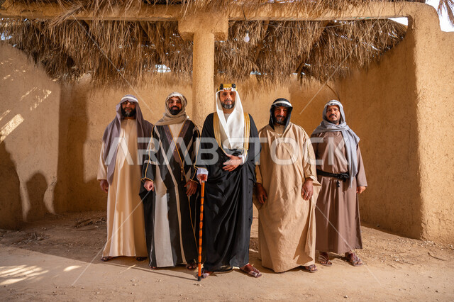 إيماءات الثقة والفخر بإنجازات المملكة، ذكرى تأسيس الدولة السعودية الأولى 1727م، إظهار الولاء والحب للوطن, مجموعة رجال عرب خليجين سعوديين يرتدون الزي الشعبي التقليدي في المناسبة الوطنية يقفون في بيت من الطين ينظرون إلى الكاميرا بتعابير الشموخ، يوم بدينا 22 فبراير