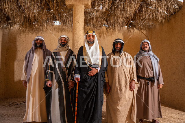 يوم بدينا 22 فبراير، إيماءات الثقة والفخر بإنجازات المملكة، ذكرى تأسيس الدولة السعودية الأولى 1727م، إظهار الولاء والحب للوطن, مجموعة رجال عرب خليجين سعوديين يرتدون الزي الشعبي التقليدي في المناسبة الوطنية يقفون في بيت من الطين ينظرون إلى الكاميرا بتعابير الشموخ