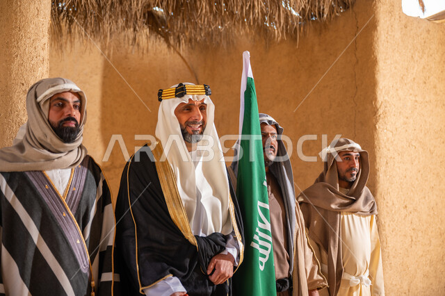 ذكرى تأسيس الدولة السعودية الأولى 1727م، يوم بدينا 22 فبراير, علم المملكة العربية السعودية، إظهار الولاء والحب للوطن, مجموعة رجال عرب خليجين سعوديين يرتدون الزي الشعبي التقليدي في المناسبة الوطنية يقفون في بيت من الطين ينظرون إلى شيء ما بإيماءات الشموخ والاعتزاز