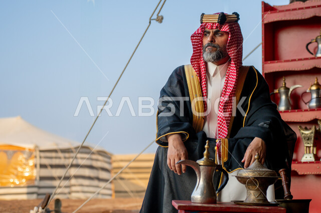  النظر الى شيء ما بتعابير الشموخ والاعتزاز والفخر، يوم بدينا 22 فبراير، الزي الشعبي في المناسبة الوطنية, إظهار حب الوطن والانتماء إليه، ذكرى تأسيس الدولة السعودية الأولى في 1727م، رجل عربي خليجي سعودي يرتدي العقال الذهبي والبشت يجلس بجوار الخيمة في الصحراء