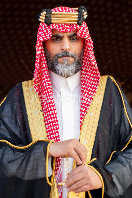 الوقوف باستقامة أمام خيمة شعبية بإيماءات الاعتزاز, حب امتلاك السيوف التراثية, صورة مقربة لرجل عربي خليجي سعودي يرتدي البشت و الشماغ التقليدي يضع يده على السيف الذهبي, التباهي بالسلاح التقليدي السعودي, يوم بدينا 22 فبراير، ذكرى تأسيس الدوله السعوديه الاولى 1727م