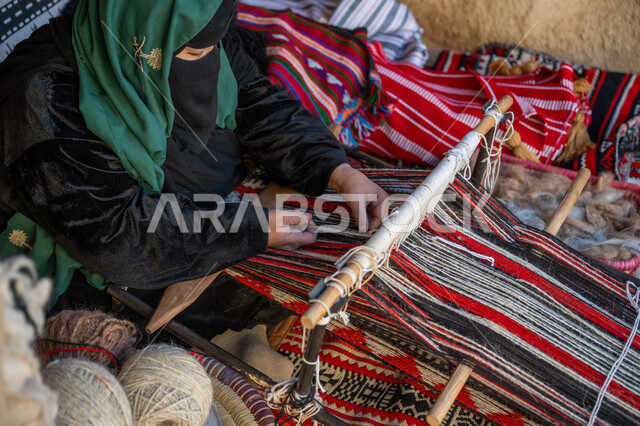 حرفة يدوية تاريخية, مهنة تقليدية قديمة, يوم بدينا  22 فبراير، ارتداء الزي الشعبي في المناسبة الوطنية، امرأة عربية خليجية سعودية ترتدي العباءة والبرقع تجلس داخل بيت من الطين تقوم بحياكة وغزل الأنسجة والقماش, منتج محلي وطني، ذكرى تأسيس الدولة السعودية الأولى في 1727م