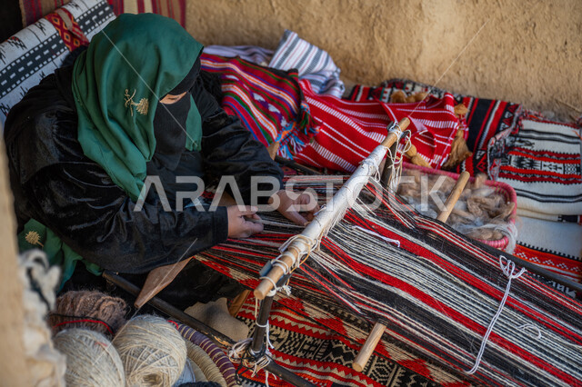 حرفة يدوية تاريخية, مهنة تقليدية قديمة, يوم بدينا  22 فبراير، ارتداء الزي الشعبي في المناسبة الوطنية، امرأة عربية خليجية سعودية ترتدي العباءة والبرقع تجلس داخل بيت من الطين تقوم بحياكة وغزل الأنسجة والقماش, منتج محلي وطني، ذكرى تأسيس الدولة السعودية الأولى في 1727م
