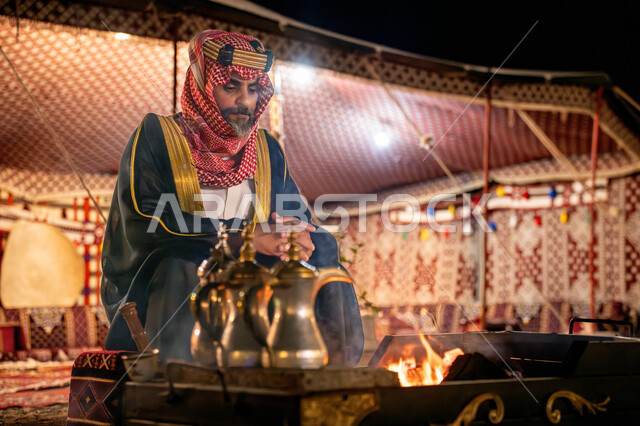 النظر الى شيء ما بتعابير الفخر, مناسبة و احتفال وطني, خيمة شعبية في الصحراء، يوم بدينا 22 فبراير، ذكرى تاسيس الدوله السعوديه الاولى 1727م, رجل عربي خليجي سعودي يرتدي البشت و الشماغ التقليدي يجلس أمام شعلة النار، اجواء شتوية ليلية