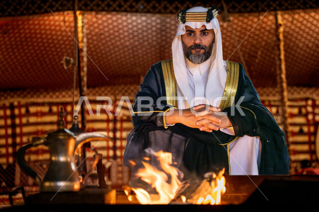 مناسبة و احتفال وطني, خيمة شعبية في الصحراء، يوم بدينا 22 فبراير، ذكرى تاسيس الدوله السعوديه الاولى 1727م, رجل عربي خليجي سعودي يرتدي البشت و الشماغ التقليدي يجلس أمام شعلة النار، اجواء شتوية ليلية