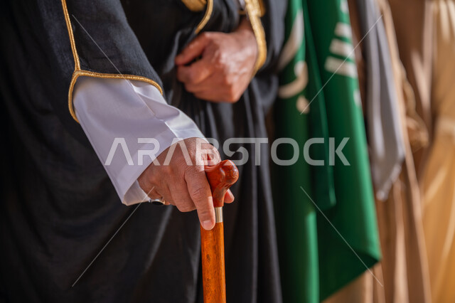 The day we started is February 22, love of the homeland and belonging to it, a close-up photo of a Saudi Arabian Gulf man wearing a bisht holding a cane in his hand standing next to the flag of the Kingdom of Saudi Arabia, wearing the traditional costume on the national occasion, the anniversary of the founding of the first Saudi state 1727 AD, pride and honor in the country's achievements