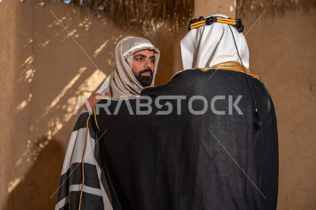 ذكرى تأسيس الدولة السعودية الأولى في 1727م، الشموخ والاعتزاز والفخر، صورة من الخلف لرجل عربي خليجي سعودي يرتدي الزي الشعبي في المناسبة الوطنية يقف في منزل من الطين يضع يده على كتف صديقه, يوم بدينا 22 فبراير، إظهار حب الوطن والانتماء إليه