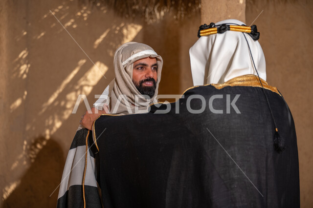 ذكرى تأسيس الدولة السعودية الأولى في 1727م، الشموخ والاعتزاز والفخر، صورة من الخلف لرجل عربي خليجي سعودي يرتدي الزي الشعبي في المناسبة الوطنية يقف في منزل من الطين يضع يده على كتف صديقه, يوم بدينا 22 فبراير، إظهار حب الوطن والانتماء إليه